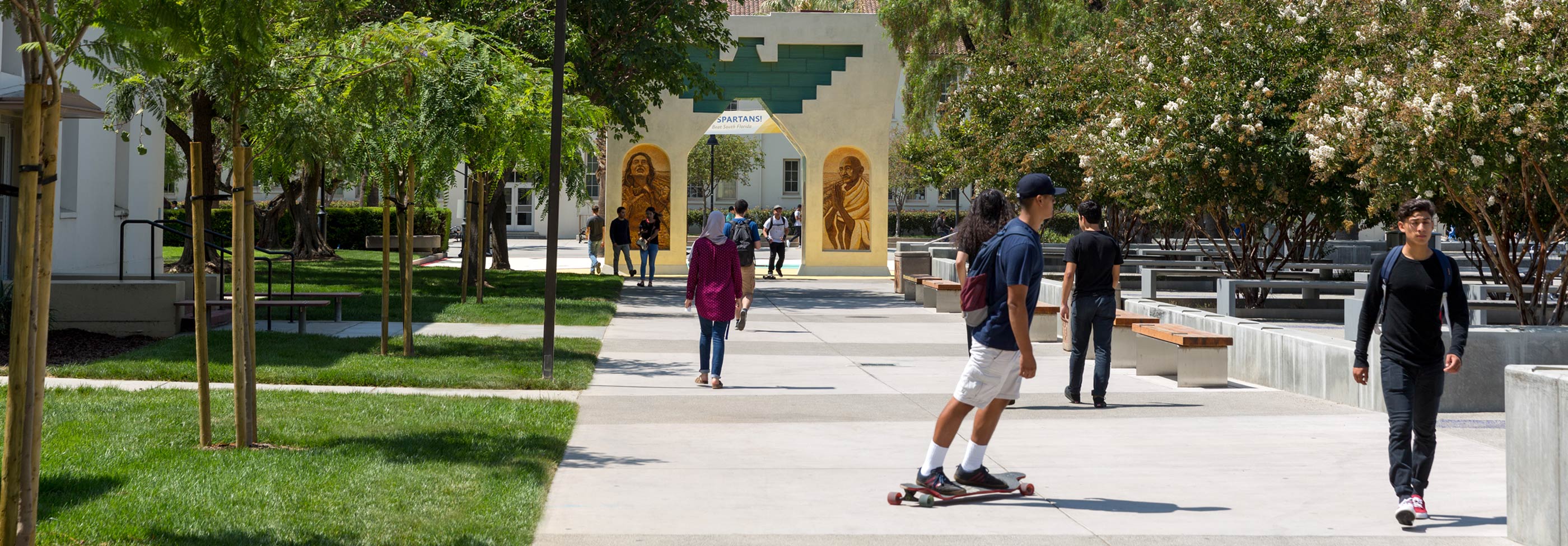 Students roaming around a lush and green campus on a sunny day.