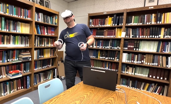 person in library with VR glasses on, immersed in what he's doing